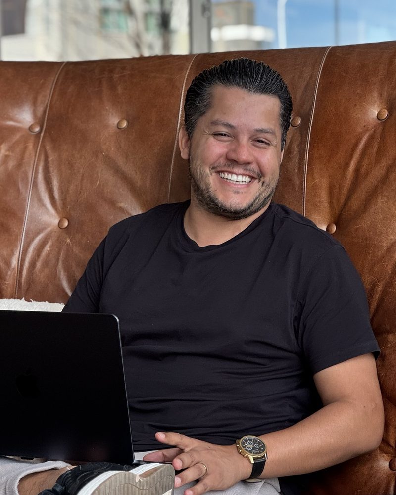 Alison Rodrigues, fundador da Virada Visual, sorrindo com o notebook no colo